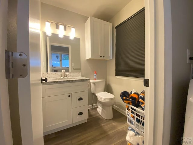 bathroom featuring vanity, baseboards, wood finished floors, and toilet