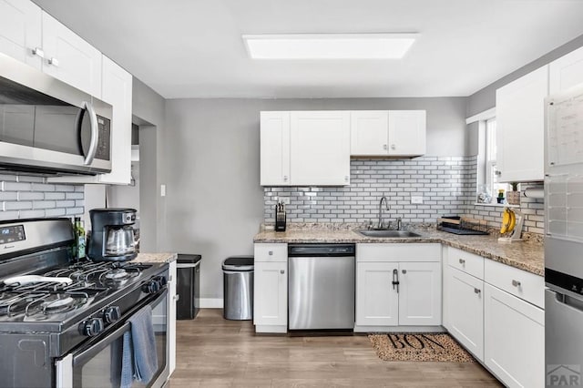 kitchen with stainless steel appliances, a sink, light stone countertops, and white cabinets