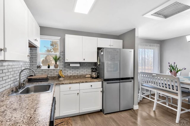 kitchen featuring visible vents, white cabinets, freestanding refrigerator, light wood-style floors, and a sink