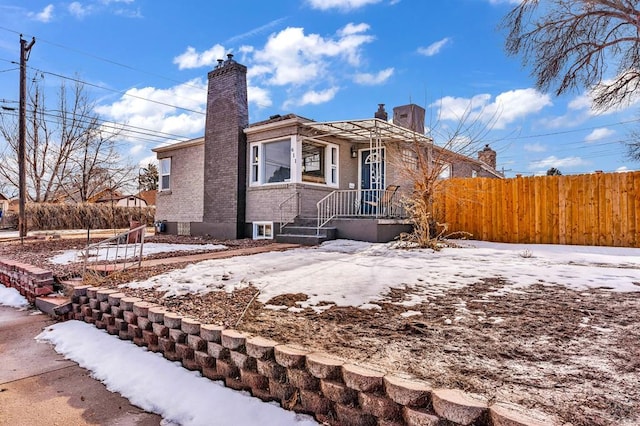 view of front facade featuring brick siding, a chimney, and fence