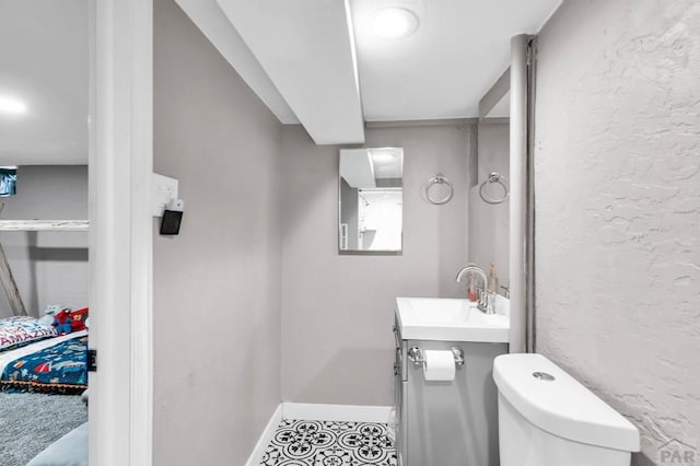 bathroom featuring toilet, a textured wall, vanity, and baseboards