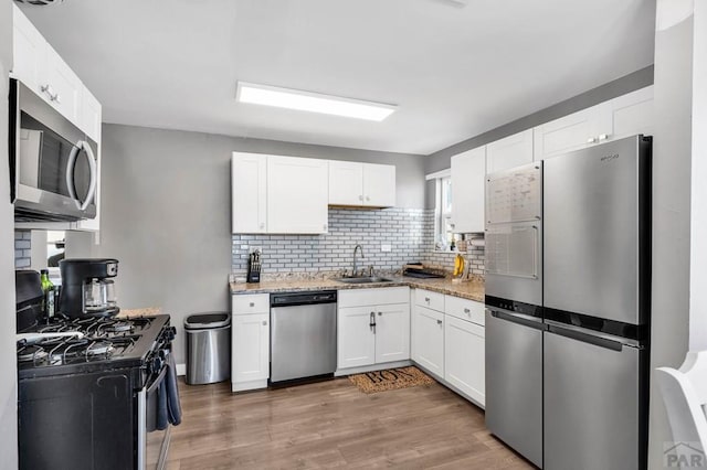 kitchen with light stone counters, stainless steel appliances, a sink, white cabinetry, and dark wood-style floors