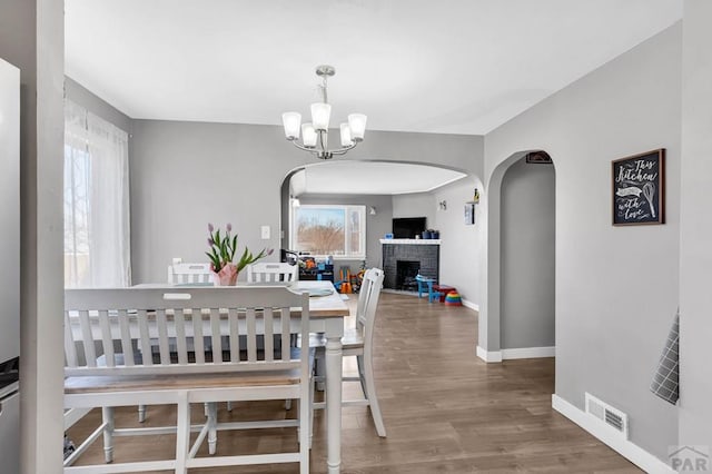 dining room featuring arched walkways, visible vents, wood finished floors, a chandelier, and baseboards