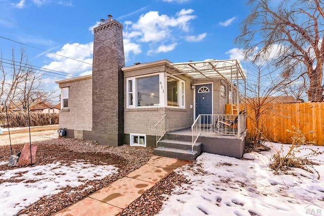 view of front of property featuring a chimney, fence, and brick siding