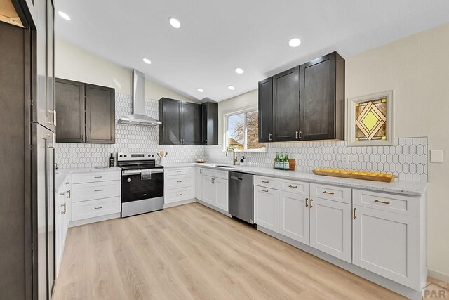 kitchen with light wood-style flooring, stainless steel appliances, lofted ceiling, a sink, and wall chimney range hood