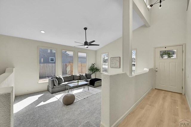 living area with baseboards, high vaulted ceiling, wood finished floors, and ceiling fan