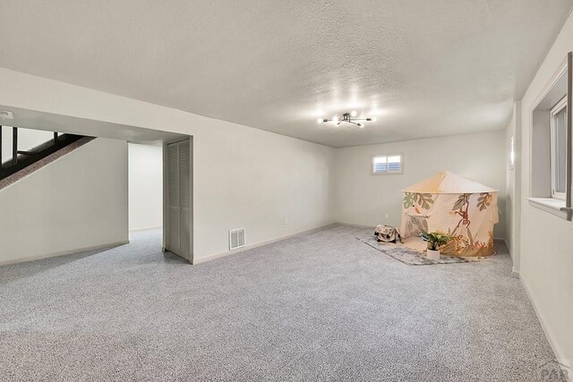 below grade area with baseboards, visible vents, carpet, and a textured ceiling