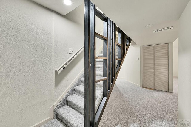 staircase with a textured wall, carpet flooring, visible vents, and baseboards