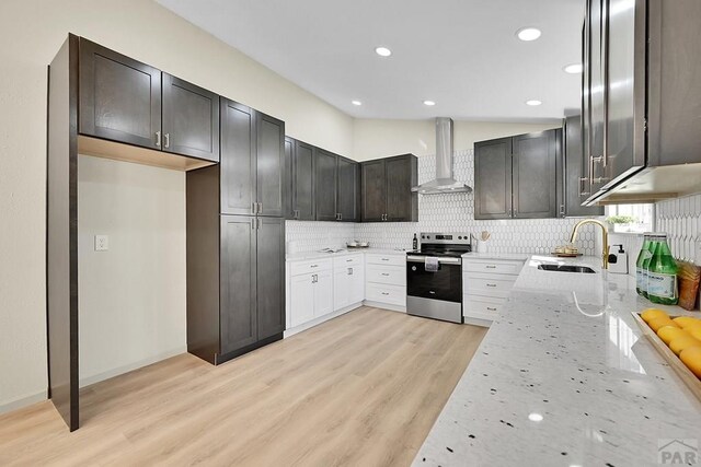 kitchen with a sink, wall chimney exhaust hood, light stone countertops, tasteful backsplash, and electric range