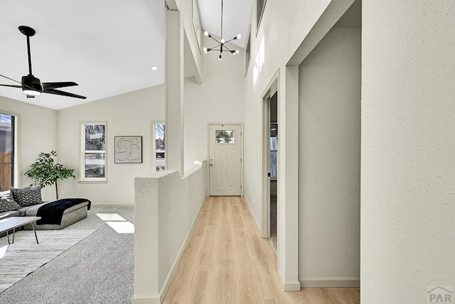 hallway with light wood-style flooring, a notable chandelier, high vaulted ceiling, and baseboards
