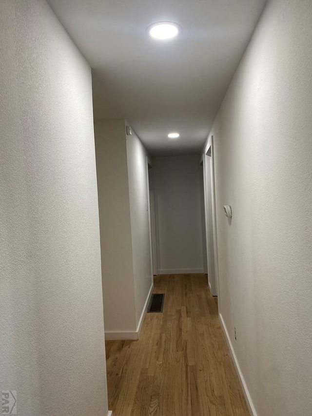 hall featuring light wood-style flooring, visible vents, and baseboards