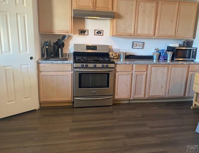 kitchen with stainless steel appliances, dark countertops, light brown cabinets, and under cabinet range hood