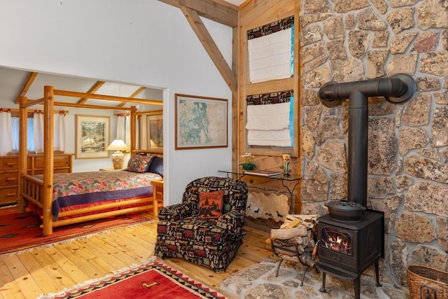 bedroom with high vaulted ceiling, a wood stove, and wood finished floors