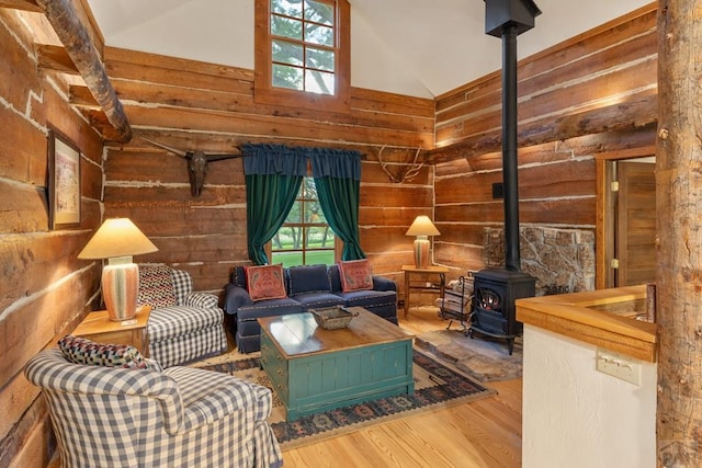 living area with high vaulted ceiling, wood finished floors, and a wood stove