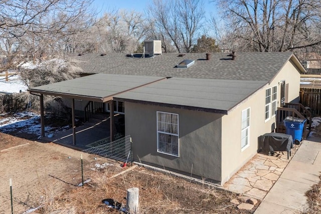 view of snowy exterior with roof with shingles, a patio area, fence, and stucco siding