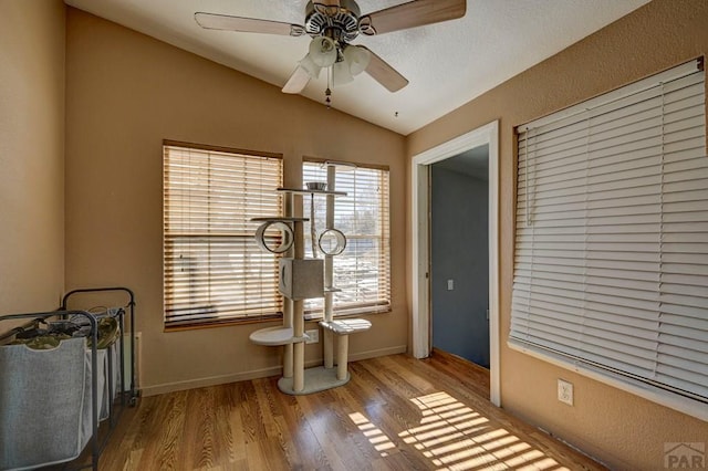 interior space featuring ceiling fan, light wood-style flooring, baseboards, and vaulted ceiling