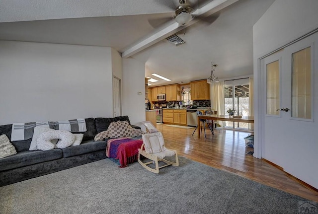 living room featuring vaulted ceiling with beams, light wood-style floors, ceiling fan, and visible vents