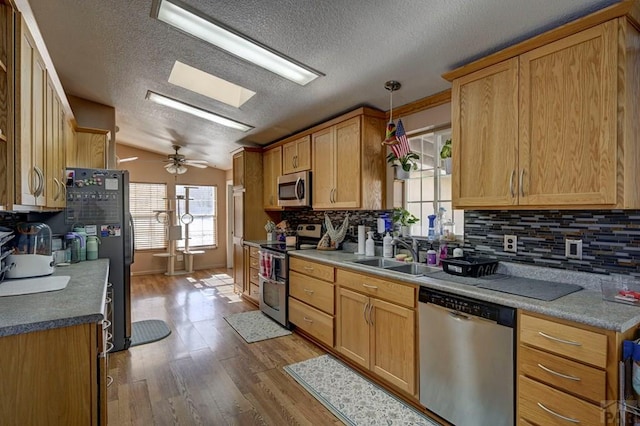 kitchen featuring pendant lighting, backsplash, appliances with stainless steel finishes, light wood-style floors, and a sink