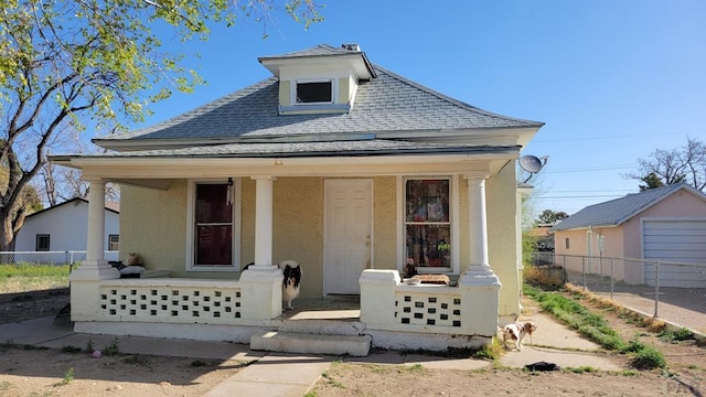 bungalow-style home featuring a porch, stucco siding, fence, and a shingled roof