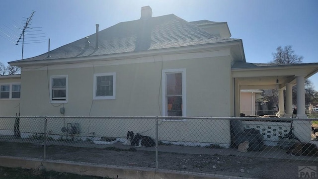 view of home's exterior with a chimney, fence, a shingled roof, and stucco siding