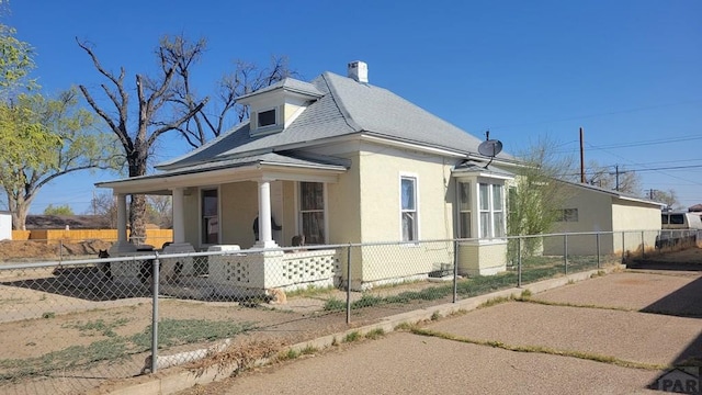 view of side of property with a fenced front yard, a shingled roof, a porch, a chimney, and stucco siding