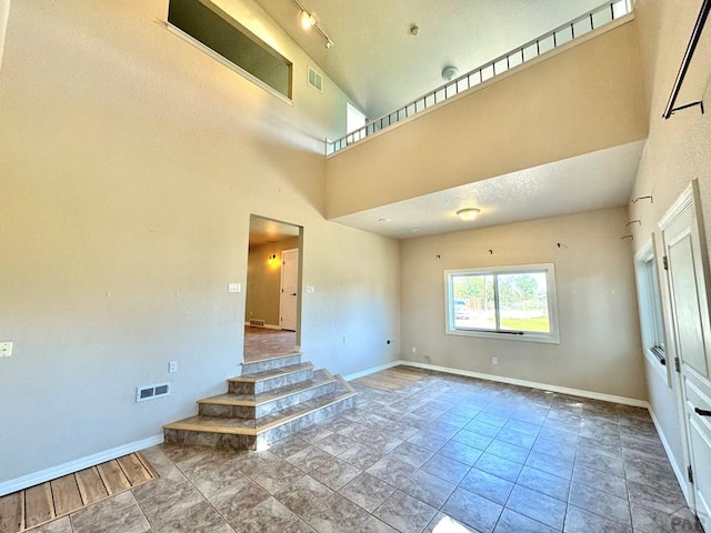 empty room with a high ceiling, visible vents, and baseboards