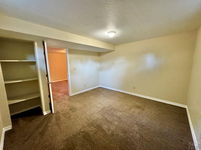 finished below grade area featuring dark carpet, a textured ceiling, and baseboards