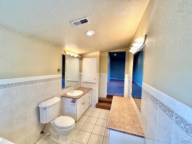 bathroom with tile walls, visible vents, a textured ceiling, vanity, and tile patterned floors