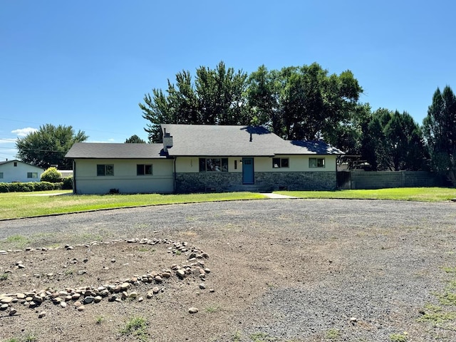 single story home with driveway, stone siding, fence, and a front yard