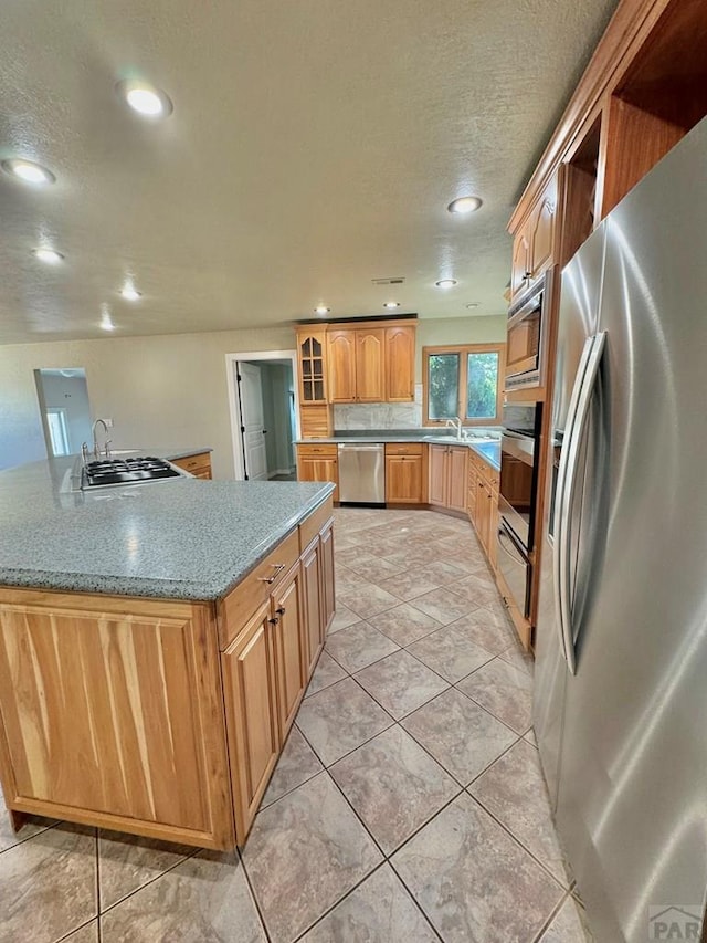 kitchen with appliances with stainless steel finishes, recessed lighting, glass insert cabinets, and a sink