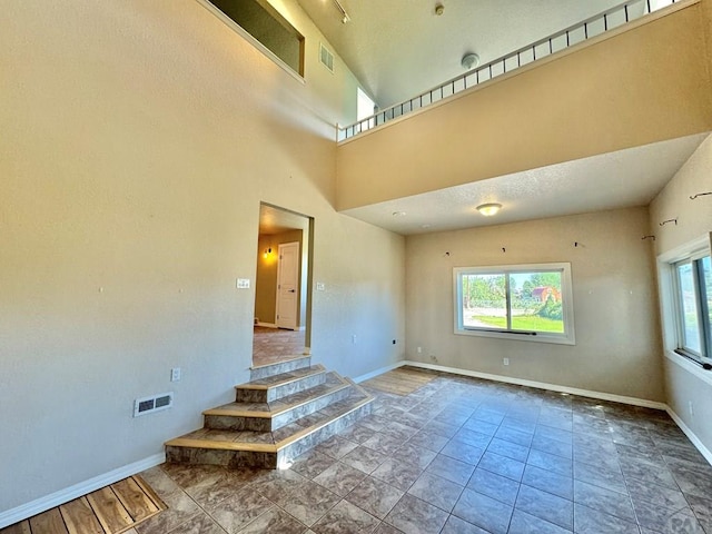 empty room featuring a towering ceiling, baseboards, and visible vents