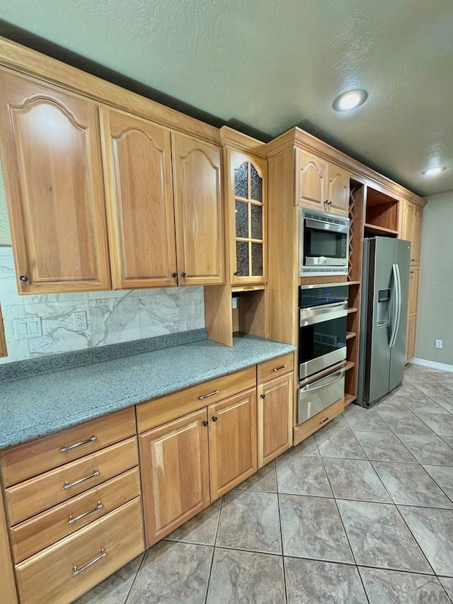 kitchen with light tile patterned floors, light countertops, appliances with stainless steel finishes, decorative backsplash, and a warming drawer