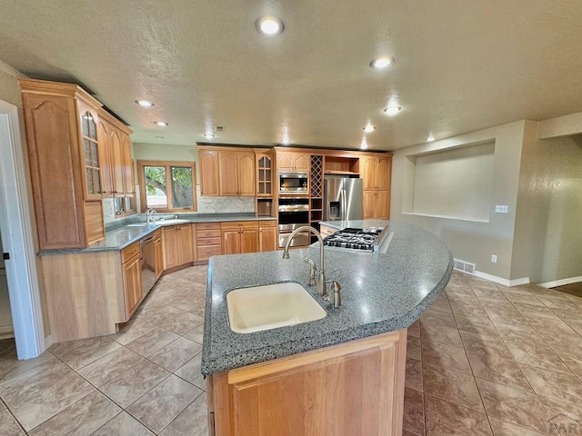 kitchen with appliances with stainless steel finishes, a center island with sink, a sink, and glass insert cabinets