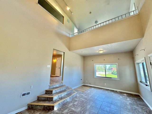 empty room featuring visible vents, a towering ceiling, and baseboards