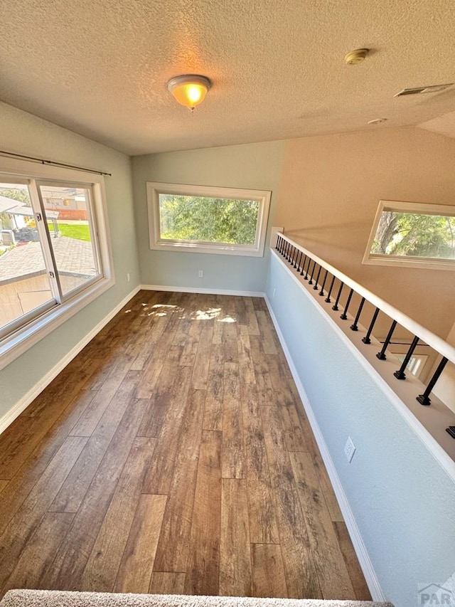 unfurnished room featuring stairs, a healthy amount of sunlight, baseboards, and wood finished floors