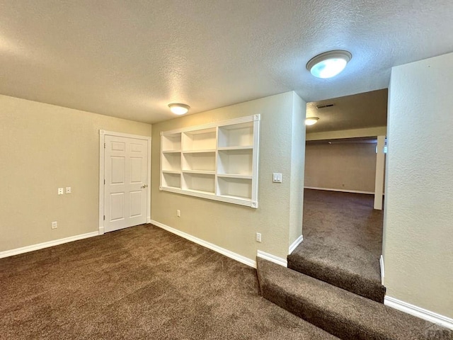 spare room featuring baseboards, built in features, a textured wall, a textured ceiling, and dark carpet