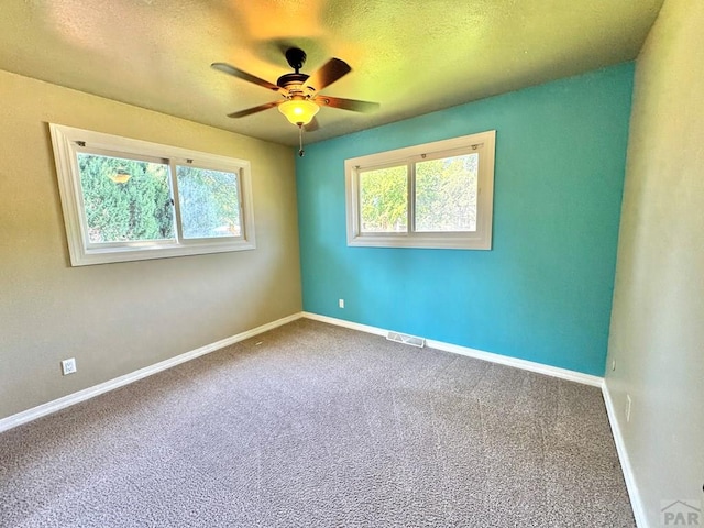 carpeted empty room with a ceiling fan, visible vents, a textured ceiling, and baseboards