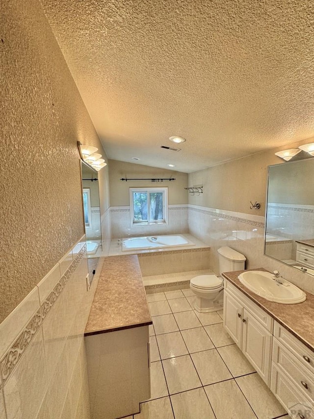 full bath featuring a textured ceiling, tile patterned flooring, a garden tub, a wainscoted wall, and tile walls