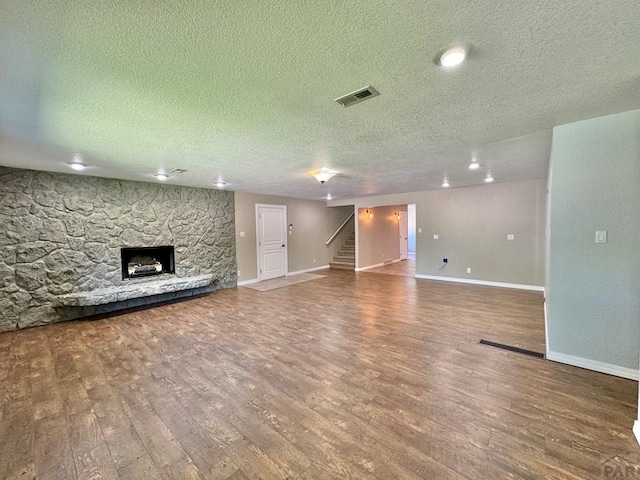 unfurnished living room featuring stairs, a fireplace, visible vents, and wood finished floors