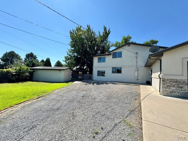 rear view of house featuring a lawn, gravel driveway, and stucco siding