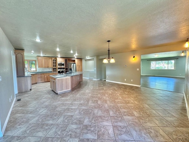 kitchen with open floor plan, stainless steel appliances, a center island with sink, and decorative light fixtures