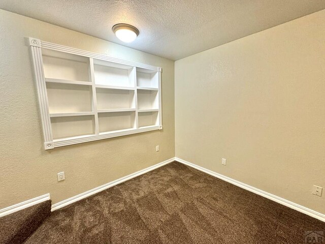 unfurnished room featuring baseboards, dark colored carpet, and a textured ceiling