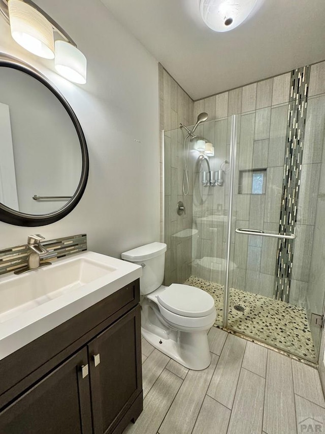 bathroom featuring wood tiled floor, toilet, vanity, and a shower stall