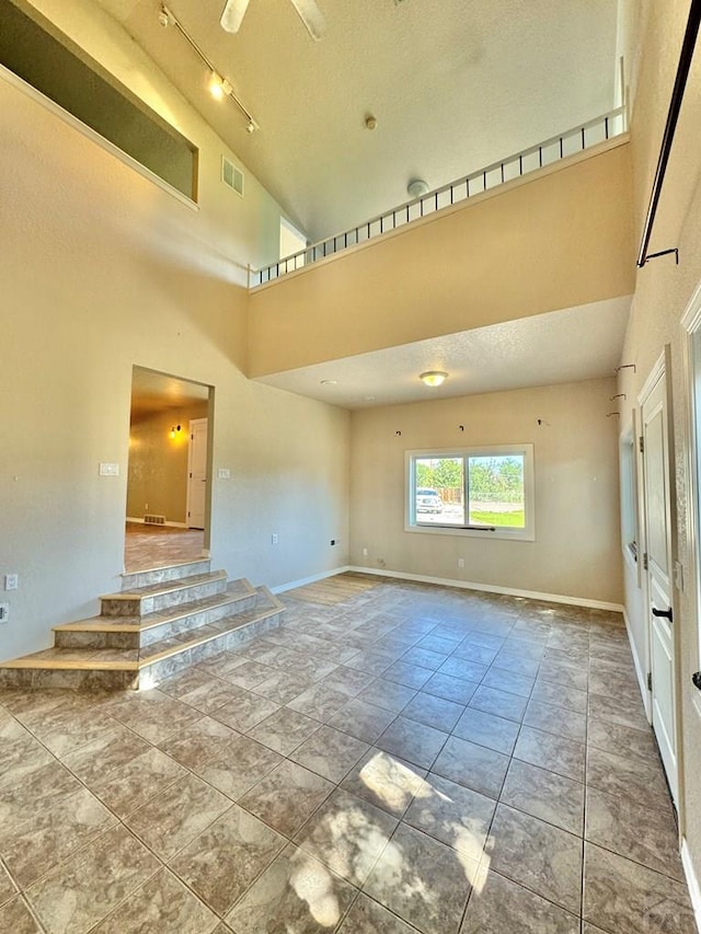 spare room with baseboards, a high ceiling, visible vents, and track lighting