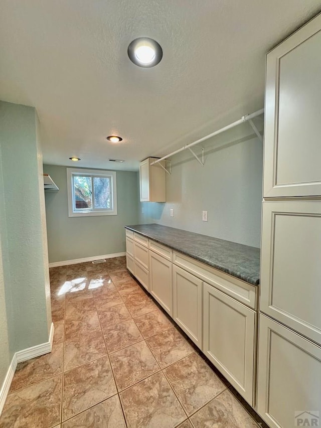 kitchen with light tile patterned floors, open shelves, dark countertops, a textured ceiling, and baseboards