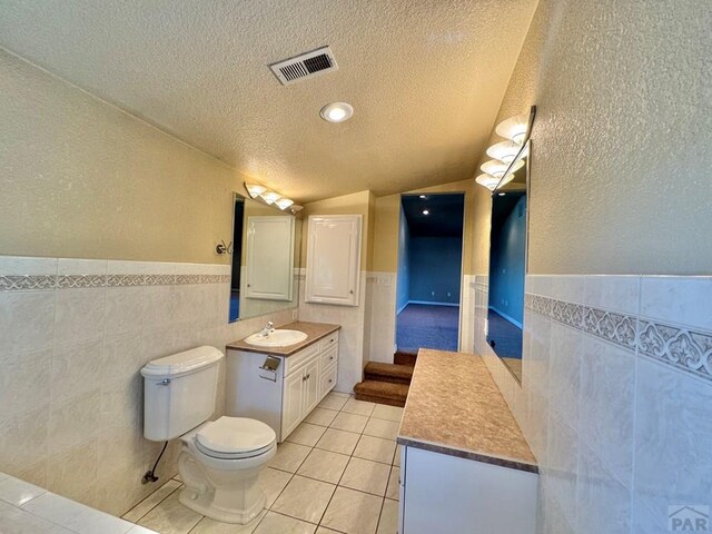 bathroom with visible vents, toilet, tile patterned floors, a textured ceiling, and tile walls