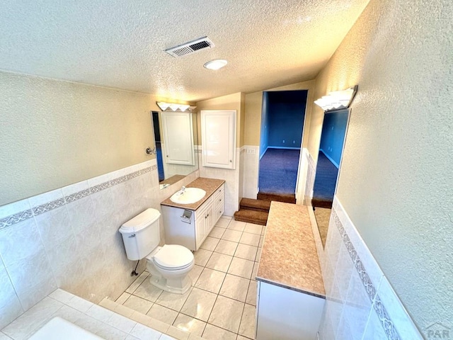 bathroom featuring a textured ceiling, tile patterned flooring, vanity, visible vents, and tile walls