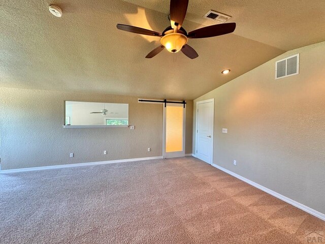 carpeted spare room with lofted ceiling, a barn door, visible vents, and baseboards