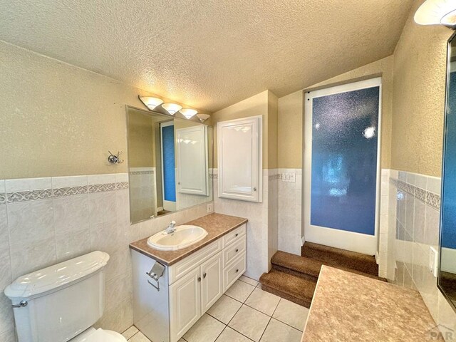 bathroom featuring toilet, tile patterned flooring, a textured ceiling, vanity, and tile walls