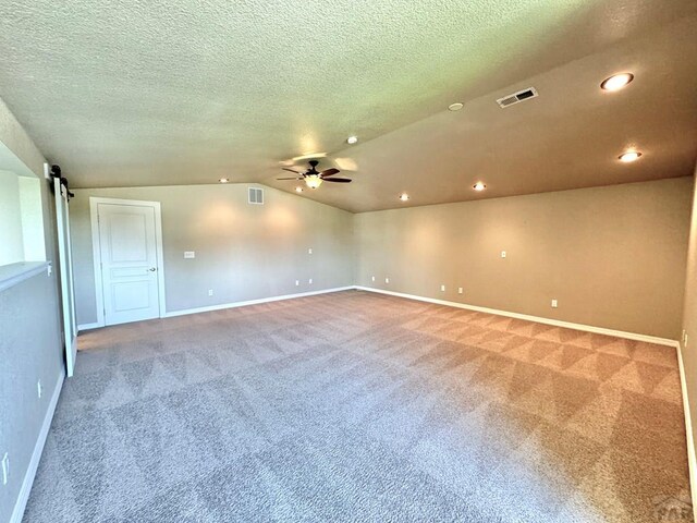 spare room featuring a barn door, visible vents, ceiling fan, vaulted ceiling, and carpet flooring